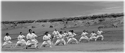 Photo of group of people practicing bojutsu on a beach